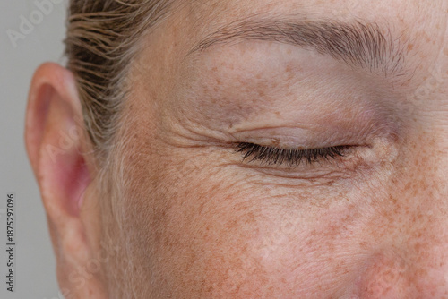 Close up cropped view of a middle aged smiling woman with wrinkles around her closed eye