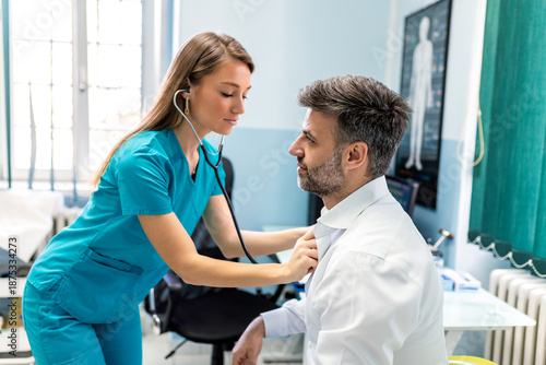 Bild auf Leinwand Female doctor in blue scrubs using stethoscope to listen to male patient's heart