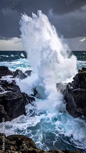 A powerful wave crashes against dark, rocky coastline under a stormy sky, creating a dramatic, dynamic waterscape