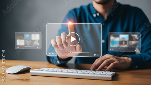 Digital media consumption concept: Professional person tapping a holographic video screen interface floating above a modern keyboard and wooden desk, symbolizing streaming, online content, and technol