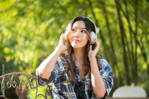 A beautiful Asian teenage girl is happily listening to music with headphones.
