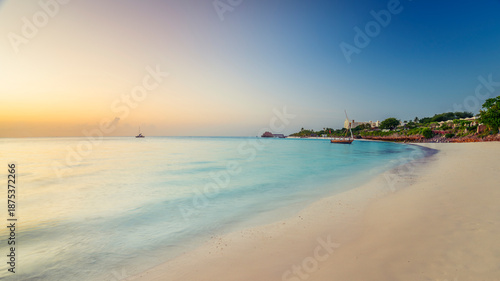 Nice view of white sandy beach with  trees, umbrellas, yachts, boats, blue ocean and background thatch stilt house at sunset.Summer holiday in Kendwa, Zanzibar island. Tanzania.
