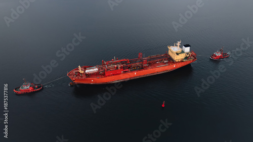 Red LPG tanker escorted by tugboats on calm sea waters, maritime transport, industrial shipping, logistics, and port operations concept.