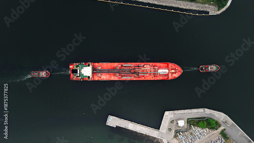 Red LPG tanker escorted by tugboats on calm sea waters, maritime transport, industrial shipping, logistics, and port operations concept.