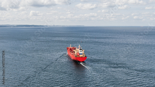 Red LPG tanker escorted by tugboats on calm sea waters, maritime transport, industrial shipping, logistics, and port operations concept.
