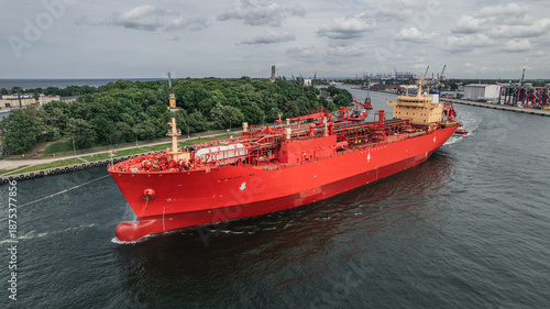 Red oil tanker escorted by tugboats on calm sea waters, maritime transport, industrial shipping, logistics, and port operations concept.