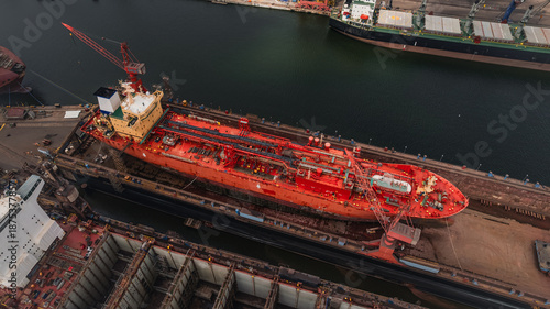Red LPG tanker escorted by tugboats on calm sea waters, maritime transport, industrial shipping, logistics, and port operations concept.
