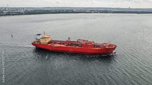 Red LPG tanker escorted by tugboats on calm sea waters, maritime transport, industrial shipping, logistics, and port operations concept.