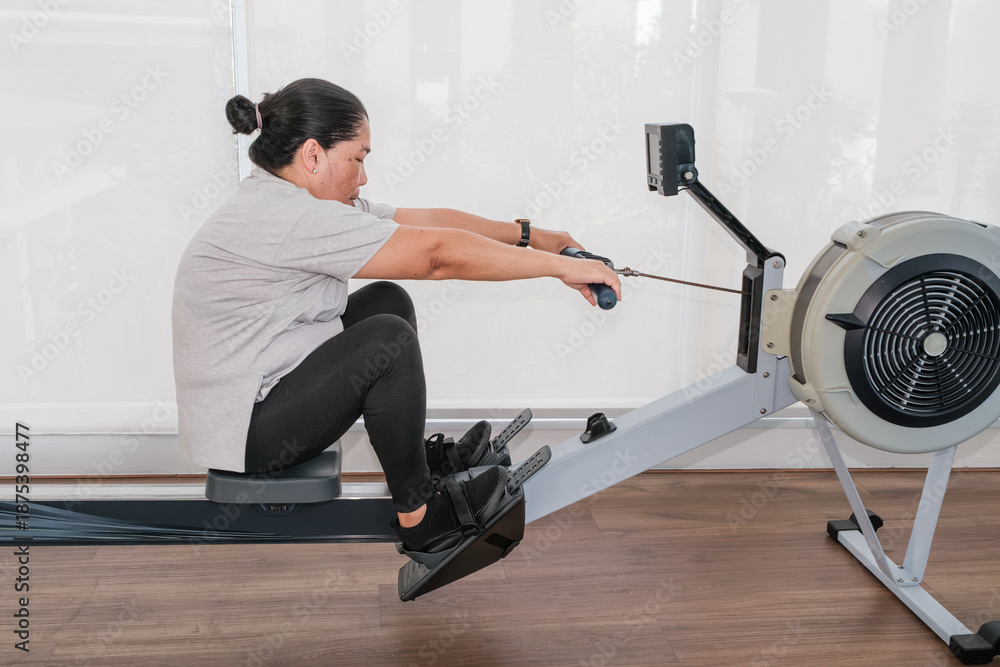 Fototapeta premium Rowing exercise in fitness studio during afternoon session near the window