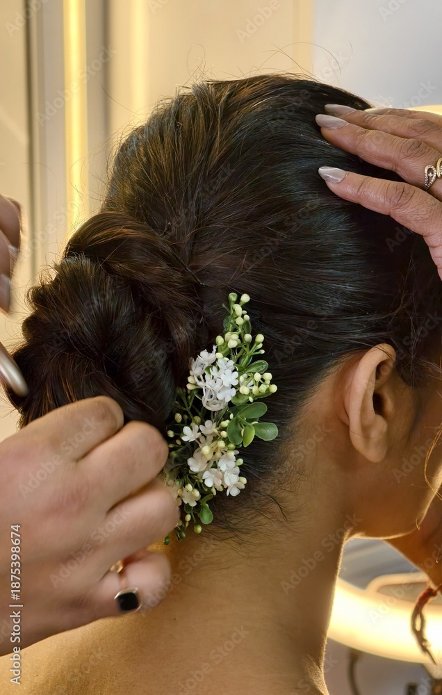 Naklejka premium Close-up of bridal hair styling with a delicate floral accessory, as a stylist secures an elegant bun during wedding preparations, highlighting craftsmanship, beauty, and traditional elegance.