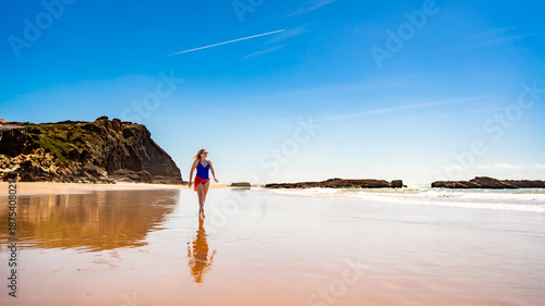 Beautiful middle-aged woman walking on sandy beach in summertime. Front view. Monte Clerigo beach on Algarve coast in Portugal	