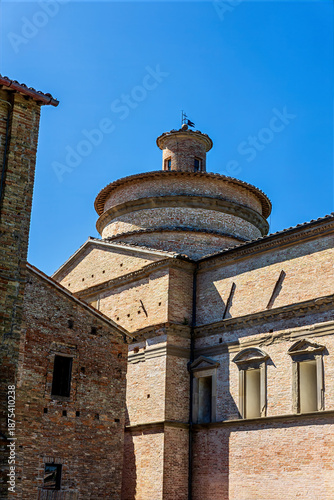 The Church of San Bernardino stands in Urbino, showcasing its Renaissance style. The structure features round elements and brickwork against a blue sky.
