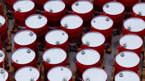 Overhead view of rows of red metal barrels with silver tops, stacked on wooden pallets
