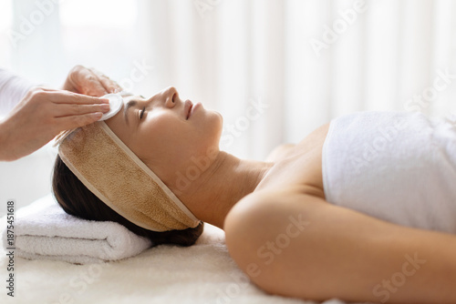 Woman enjoying facial cleansing treatment at spa, eyes closed and relaxed, minimal interior highlighting self care, skin health, and luxury wellness services.