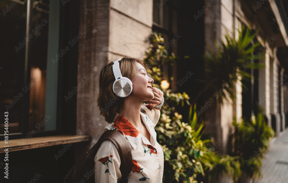 Obraz premium Asian girl in profile with headphones closes eyes and smiles, fully immersed in music, surrounded by nature, embodying serenity, balance, and tech-powered calmness.