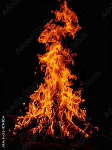 Hot burning wood logs with tall flames and glowing embers against a pitch black sky for holiday and ritual events.