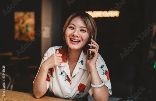 Tablou pe pânză Close-up of cheerful Asian woman holding phone and stylus, expressing happiness, connection, and creative communication in modern freelance lifestyle