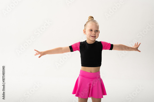 Smiling dancer with cochlear implant stretching arms in pink costume in studio. Hearing support, inclusive fitness and childhood artistic development through expressive movement