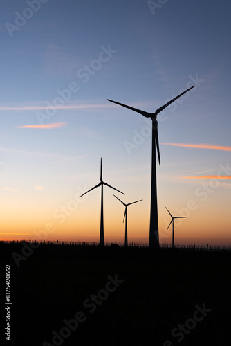 Four silhouettes of wind turbines producing wind energy at sunset