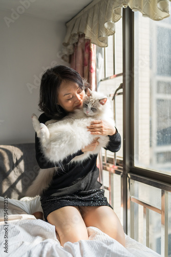  Woman Cuddling Fluffy White Ragdoll Cat by Window in Cozy Urban Apartment Bedroom Morning