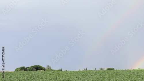 Vibrant double rainbow over a green agricultural field. Perfect for themes of hope, nature's beauty, climate, and magical natural phenomena.