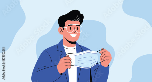 Happy young man with glasses and a blue jacket smiling as he holds a disposable medical face mask in his hands.