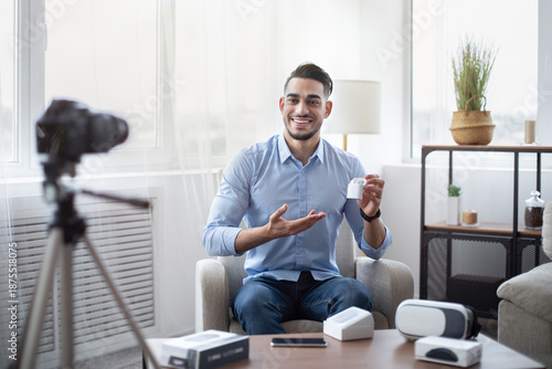 Wallpaper Mural Arab male blogger promoting new model of wireless earphones, filming video review of modern gadget at home. Famous influencer making content for his tech channel, recommending innovative product Torontodigital.ca