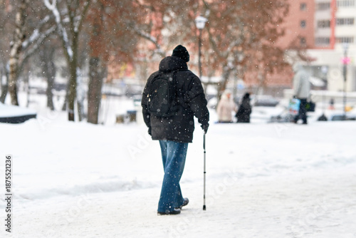Картината върху платно Snowflakes in focus and the blurred figure of an elderly man walking slowly through falling snow with cane and backpack, navigating snow covered sidewalk