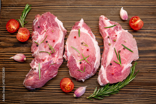 Top view of three steaks of raw fresh meat with spices on a wooden table. Pork meat texture.