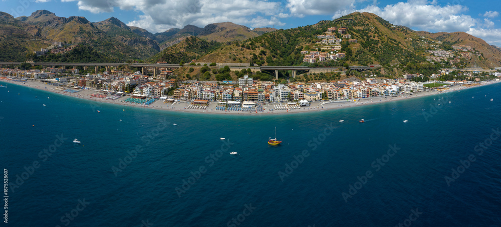 Fototapeta premium Aerial view of the small town of Letojanni, in the province of Messina, Sicily, Italy. It is a Sicilian coastal town and a beautiful tourist destination. In foreground is the blue Mediterranean Sea.