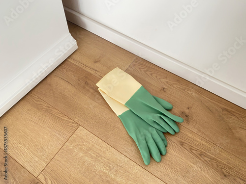 A pair of rubber cleaning gloves lying on a wooden floor near furniture in an interior space