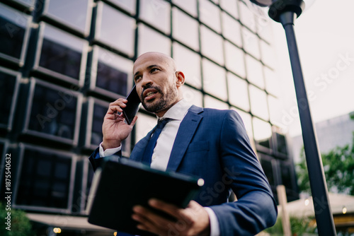 Cuadro en lienzo Professional businessman communicating on smartphone and holding tablet, speaking assertively, embodying mobile control, leadership and fast decision-making in corporate tech world