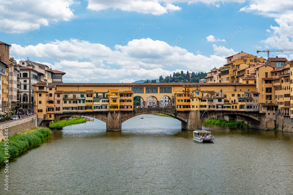 Obraz premium View of Ponte Vecchio in Florence (Ponte Vecchio, Firenze) and nearby buildings along the Arno River on a bright summer day, capturing the historic charm and vibrant riverside scene.