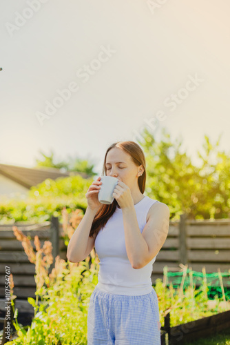 Young woman drinking coffee while standing against sky in the garden
