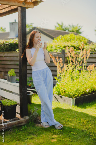 Young woman drinking coffee while standing against sky in the garden