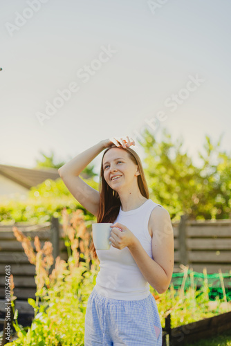 Young woman drinking coffee while standing against sky in the garden