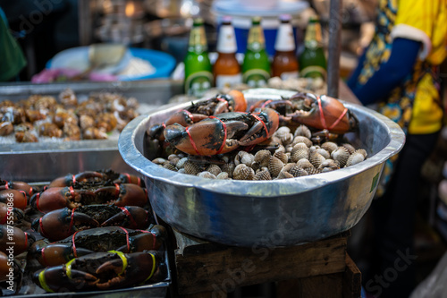 Live crabs stacked on a tray at a Thai street food stall, their claws tied as they wait for sale, capturing the raw and authentic atmosphere of local market life.