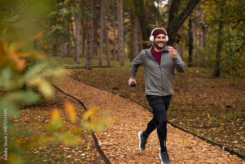 Bild auf Leinwand Man jogging outdoors wearing headphones in autumn park