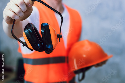 Photos Worker presenting orange earmuffs and safety helmet