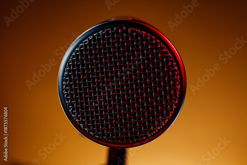 A microphone sits in focus with a metal mesh top. The background is brown with some red light. This setup often appears in recording sessions or live performances at night.
