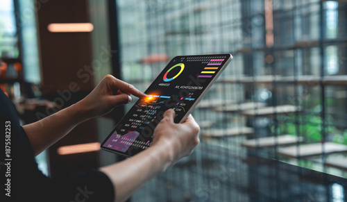 Canvas Print A person interacts with a digital tablet displaying data visuals, set against a modern, glass-walled environment