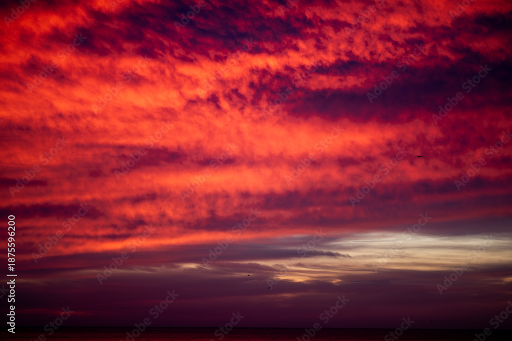 Obraz premium Fiery red sunset clouds over dark ocean horizon, dramatic evening atmosphere, travel agency or yoga apps