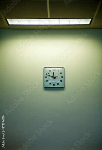Clock on an office wall under a strip light, time nearly 11.50. Clockwatching.