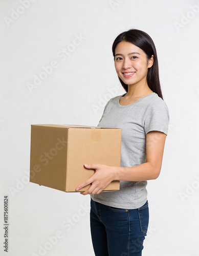 Young woman carrying a cardboard box and smiling at the camera on white background