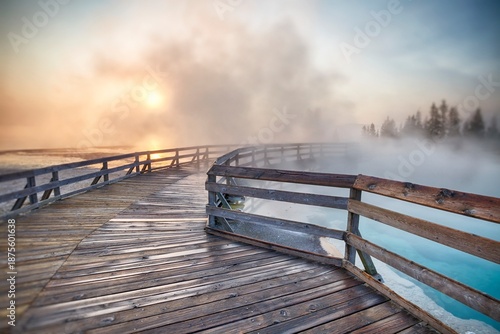 Steaming hot spring at sunrise with wooden boardwalk curving through West Thumb Geyser Basin in Yellowstone National Park.