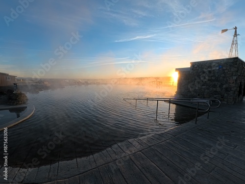 View of vaporous waters reflecting the dawn sunlight, wooden deck in the foreground, and a windmill against the brightening sky, Burns, Oregon, United States.