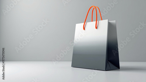 Gray gradient shopping bag with bright orange cord handles, standing on a glossy reflective surface against a plain gray backdrop, softly lit for a sleek, minimal, modern product‑focused presentation.