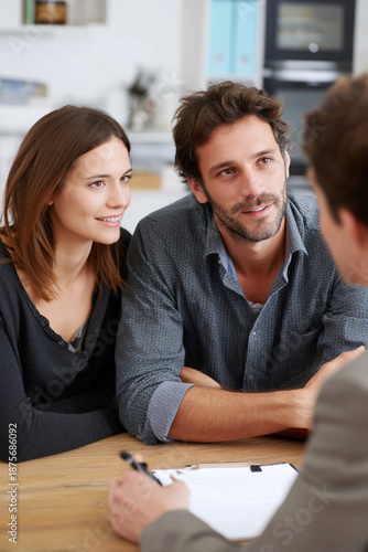 A thoughtful insurance agent is making notes while discussing life insurance options with a young couple