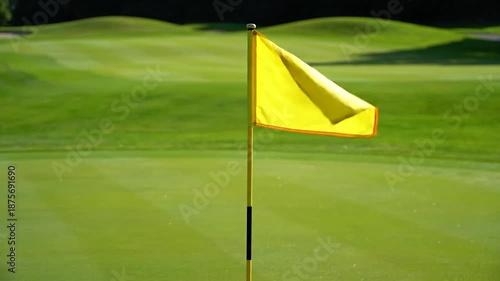 Yellow golf flag on a pole stands on a vibrant green course, sun-drenched scene
