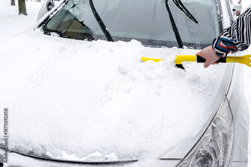 Man brushing snow and ice from windscreen of car with brush. Person cleaning fresh snow after snowstorm from car in winter